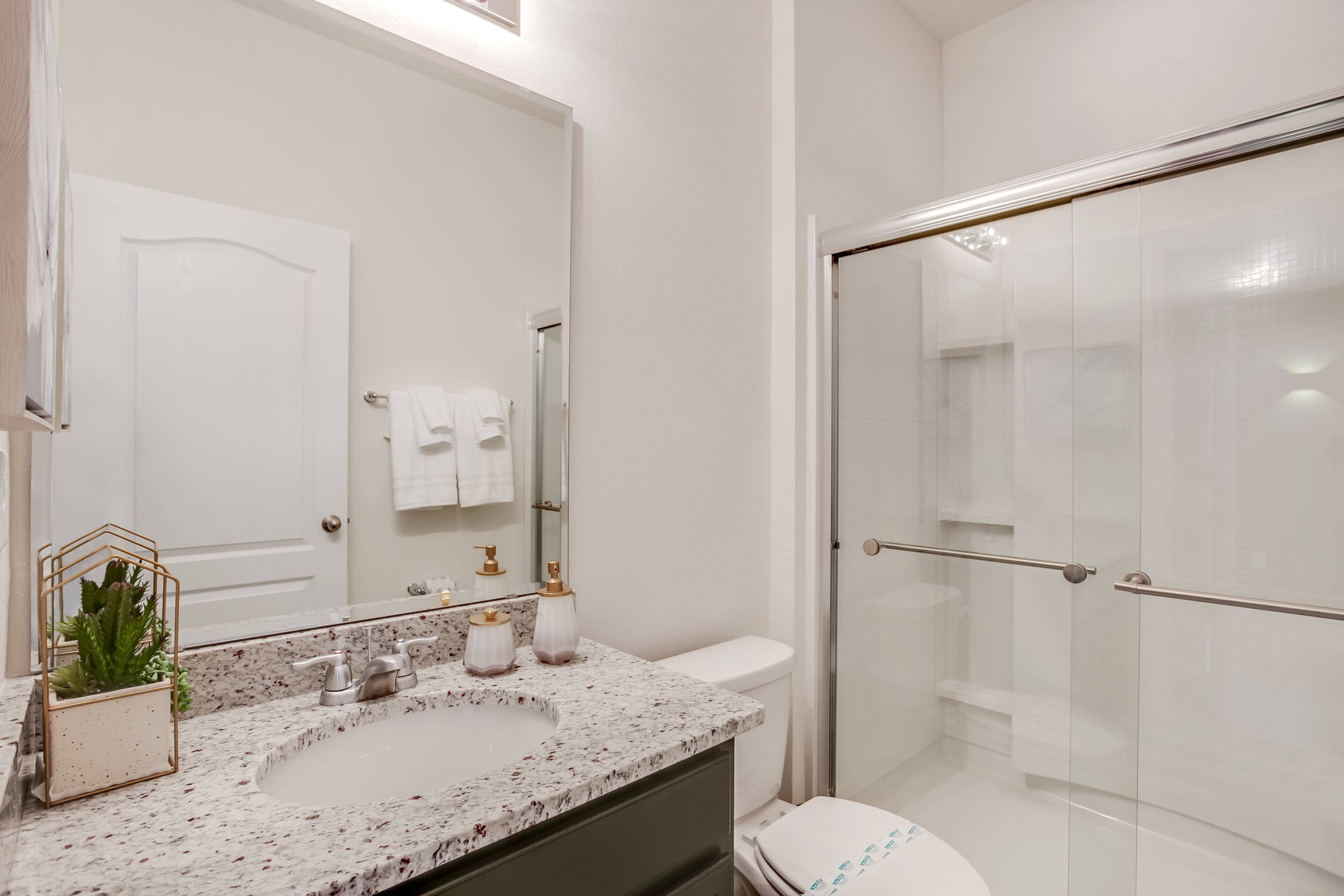 A modern bathroom with a marble sink, a glass shower enclosure, and a white toilet.