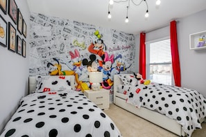 Un dormitorio con dos camas, un mural en la pared con personajes de dibujos animados y una ventana con cortinas rojas.