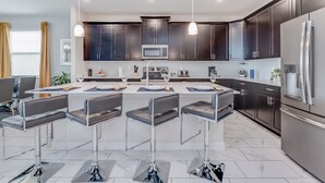 A modern kitchen with dark cabinets, stainless steel appliances, and a central island with bar stools. - 1559muligan (Davenport)