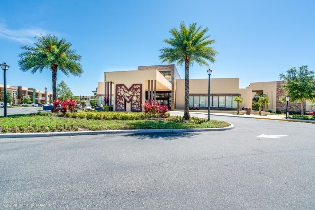 A modern building with a central entrance, palm trees, and a landscaped area with red flowers.
