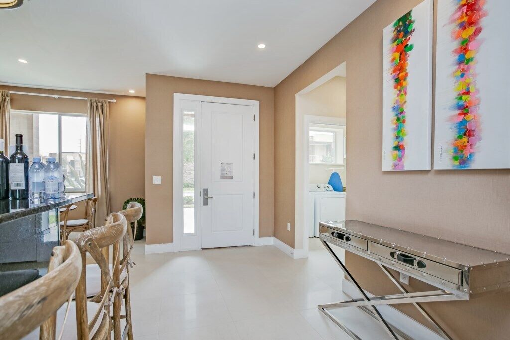 A modern kitchen with a bar area, wooden chairs, and a white door leading to another room.