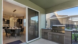 A modern kitchen with a sliding glass door leading to a dining area, a built-in grill, and a view of the backyard. - This Dream 6 Bdrm, 5 BA Home (Davenport)