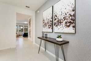 A hallway with a modern design, featuring a dark wooden console table with a potted plant, two abstract wall art pieces, and a patterned wall.