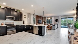 A modern kitchen with dark cabinetry, stainless steel appliances, and a marble floor. - 8 Bed 5 Ba Villa with Games, Pool & Spa (Davenport)