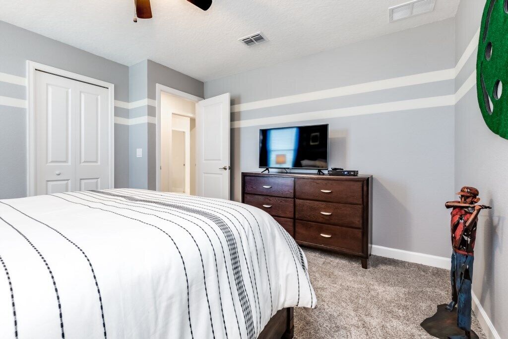 A bedroom with a bed, a dresser, and a television on the wall.