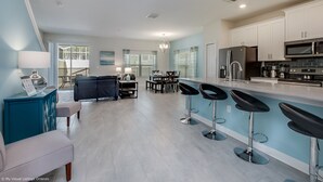 A modern kitchen with white cabinets, a black refrigerator, and a microwave. There is a dining area with a table and chairs, and a living room with a sofa and a coffee table. - 780pb Luxury Furnished 5 Bedroom 4 Bathroom (Davenport)