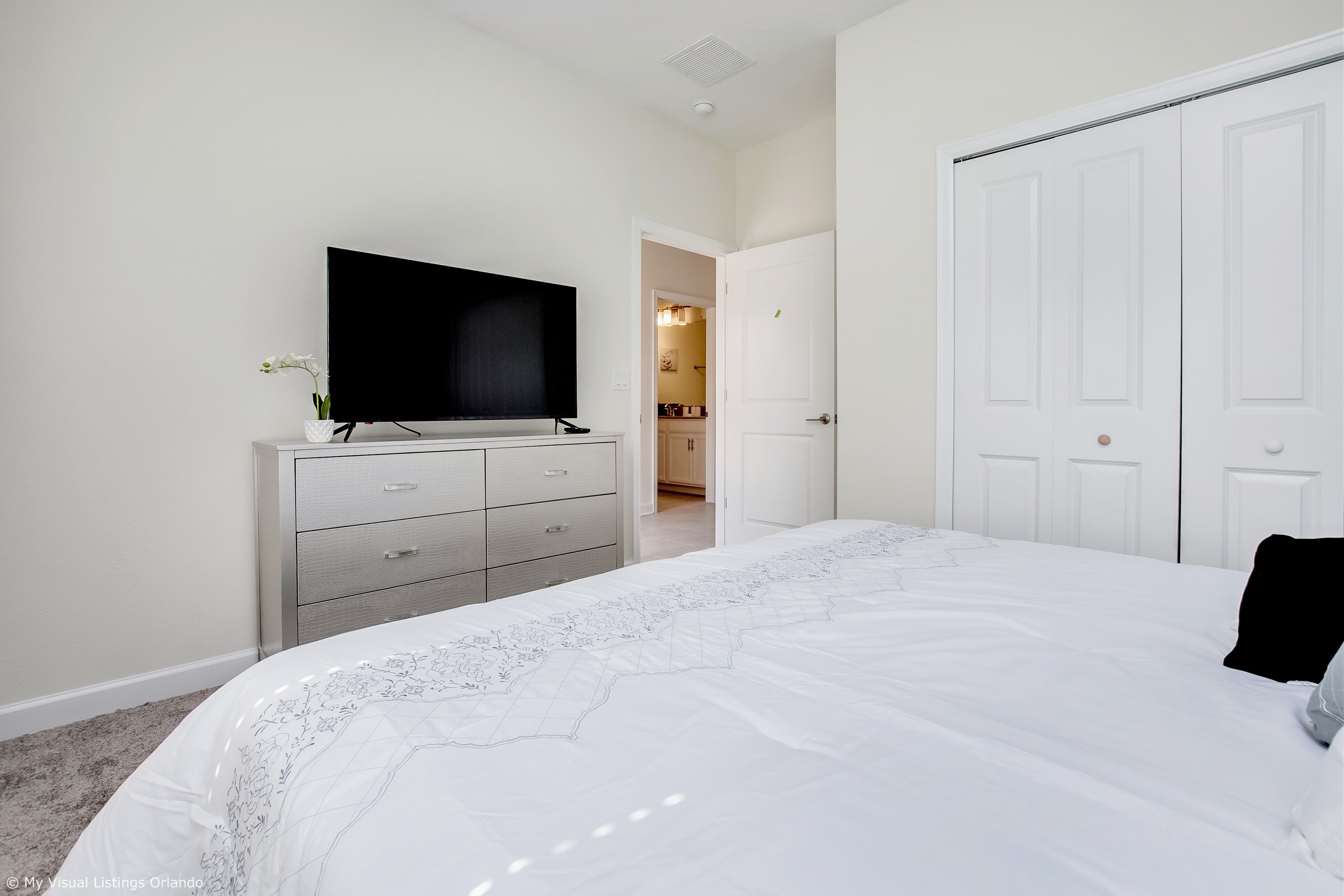 A bedroom with a large bed, a dresser, a flat-screen TV, and a closet.