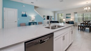 A modern kitchen with a dishwasher, a sink, and a dining area with a table and chairs. - 780pb Luxury Furnished 5 Bedroom 4 Bathroom (Davenport)