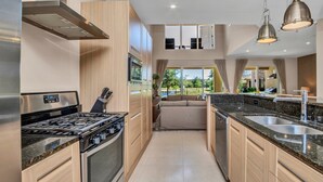 A modern kitchen with a gas stove, stainless steel appliances, wooden cabinets, and a large window offering a view of the outdoors. - Modern Magic Village Resort Townhouse 7620 (Kissimmee)