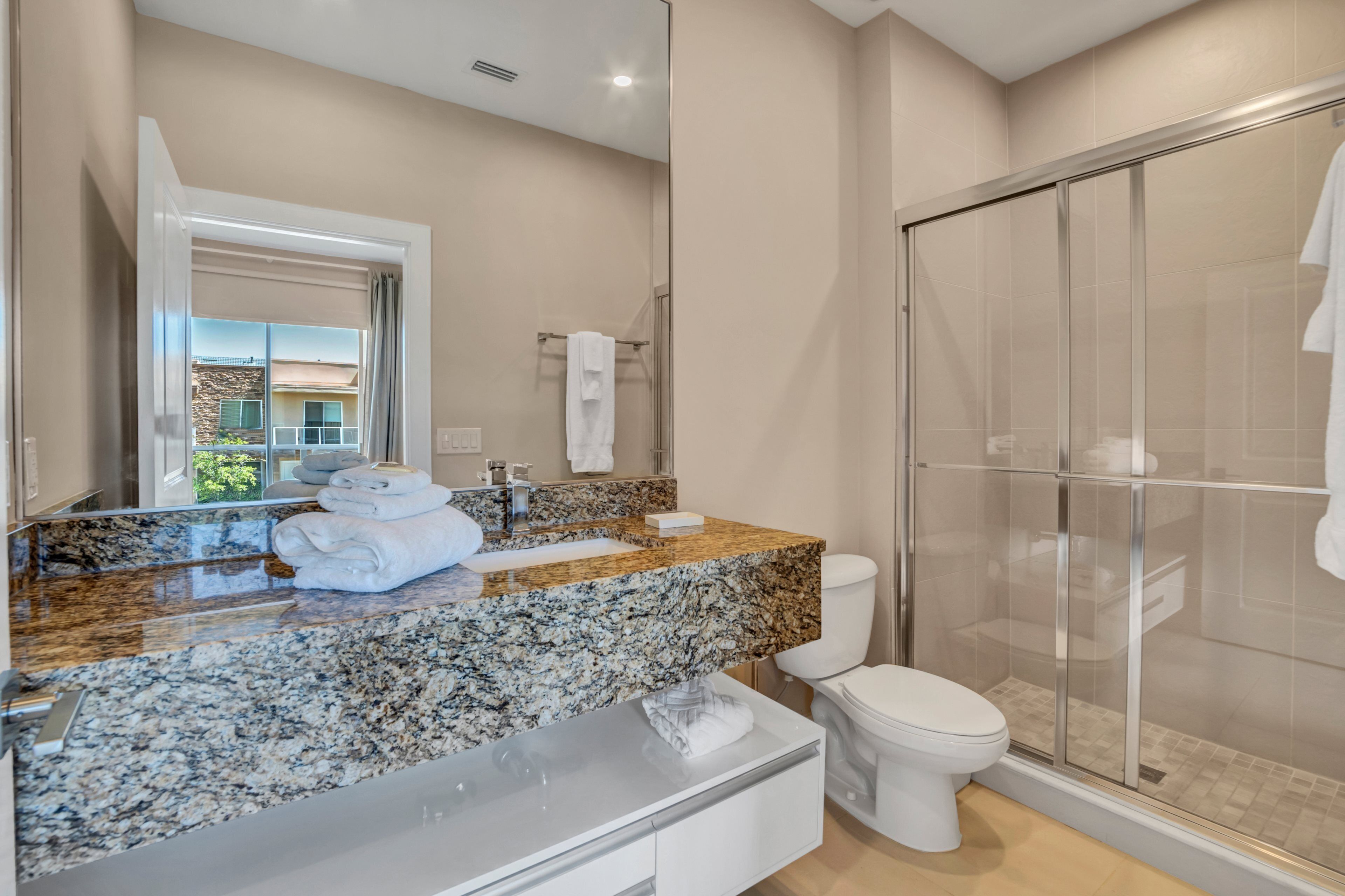 A modern bathroom with a granite countertop, a white toilet, and a glass-enclosed shower.