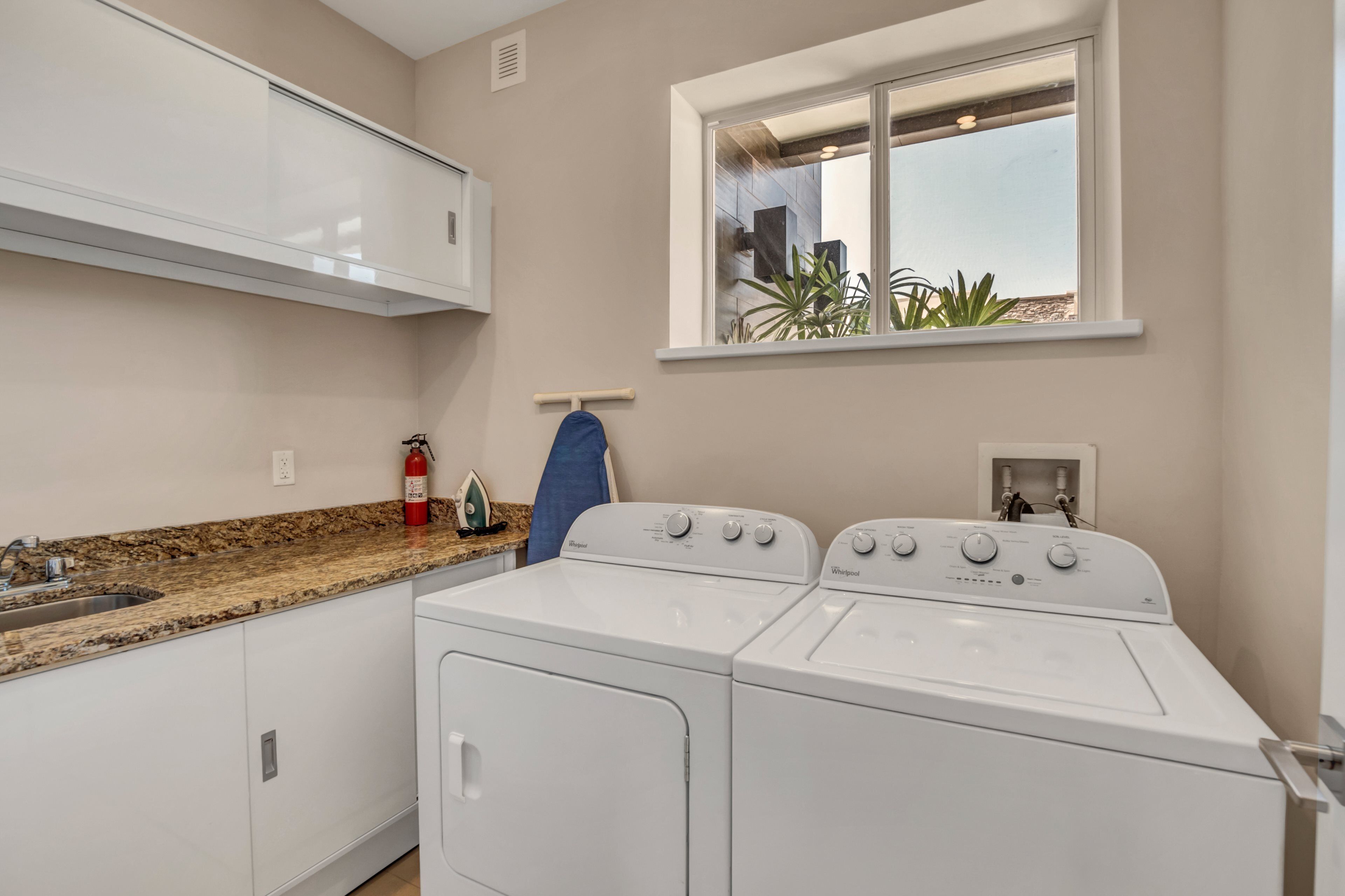 A laundry area with two white front-loading washers and dryers, a granite countertop, a window with a view of buildings, and a towel rack.