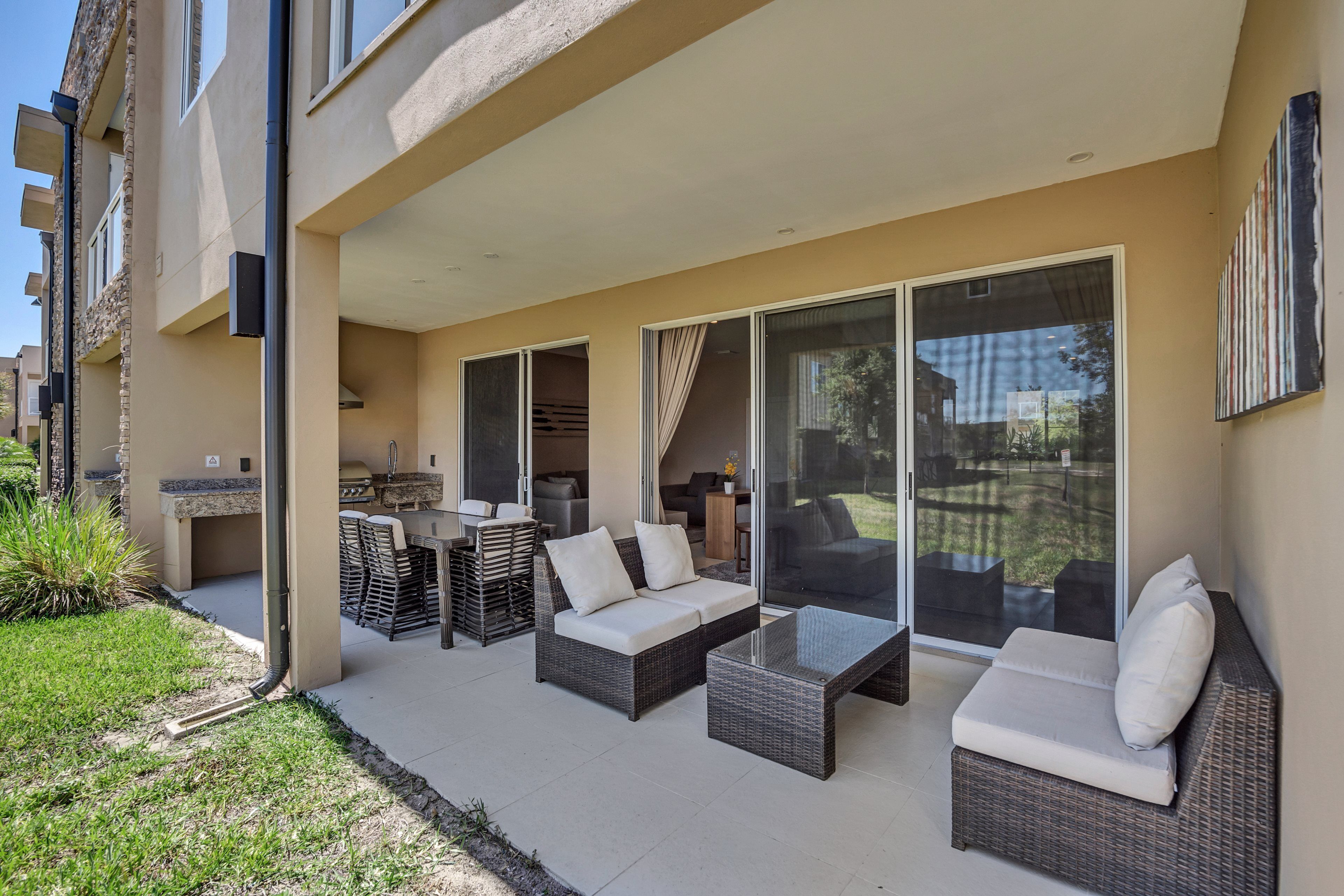 A modern outdoor living area with wicker furniture, a glass door leading to a patio, and a view of the surrounding neighborhood.