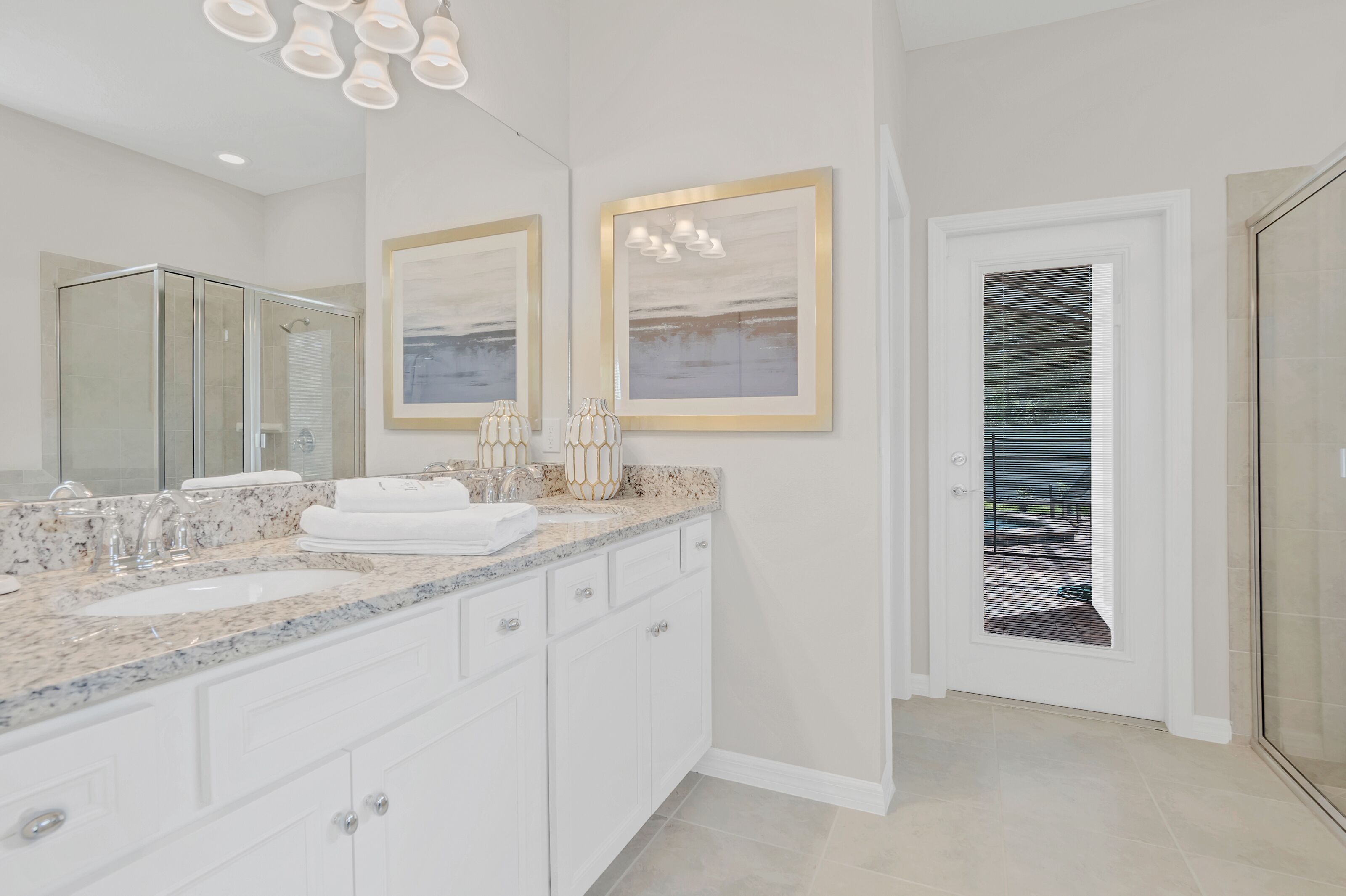 A modern bathroom with a large mirror, two framed pictures, a white vanity with a marble countertop, and a glass shower enclosure.
