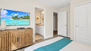 A bedroom with a bed, a TV on a wooden cabinet, a bathroom with a sink and mirror, and a door leading to another room. - 8864bengal (Kissimmee)