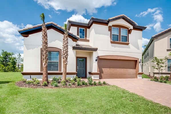 A two-story house with a garage, a front door, and a small garden with palm trees.