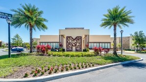 A modern building with a large decorative entrance, surrounded by palm trees and a landscaped garden. - 7605reclife (Kissimmee)
