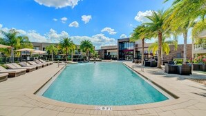 A swimming pool with lounge chairs and palm trees, surrounded by a building with a modern design. - 7605reclife (Kissimmee)