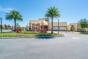 A modern building with a central entrance, palm trees, and a landscaped area with red flowers. - 7605reclife (Kissimmee)