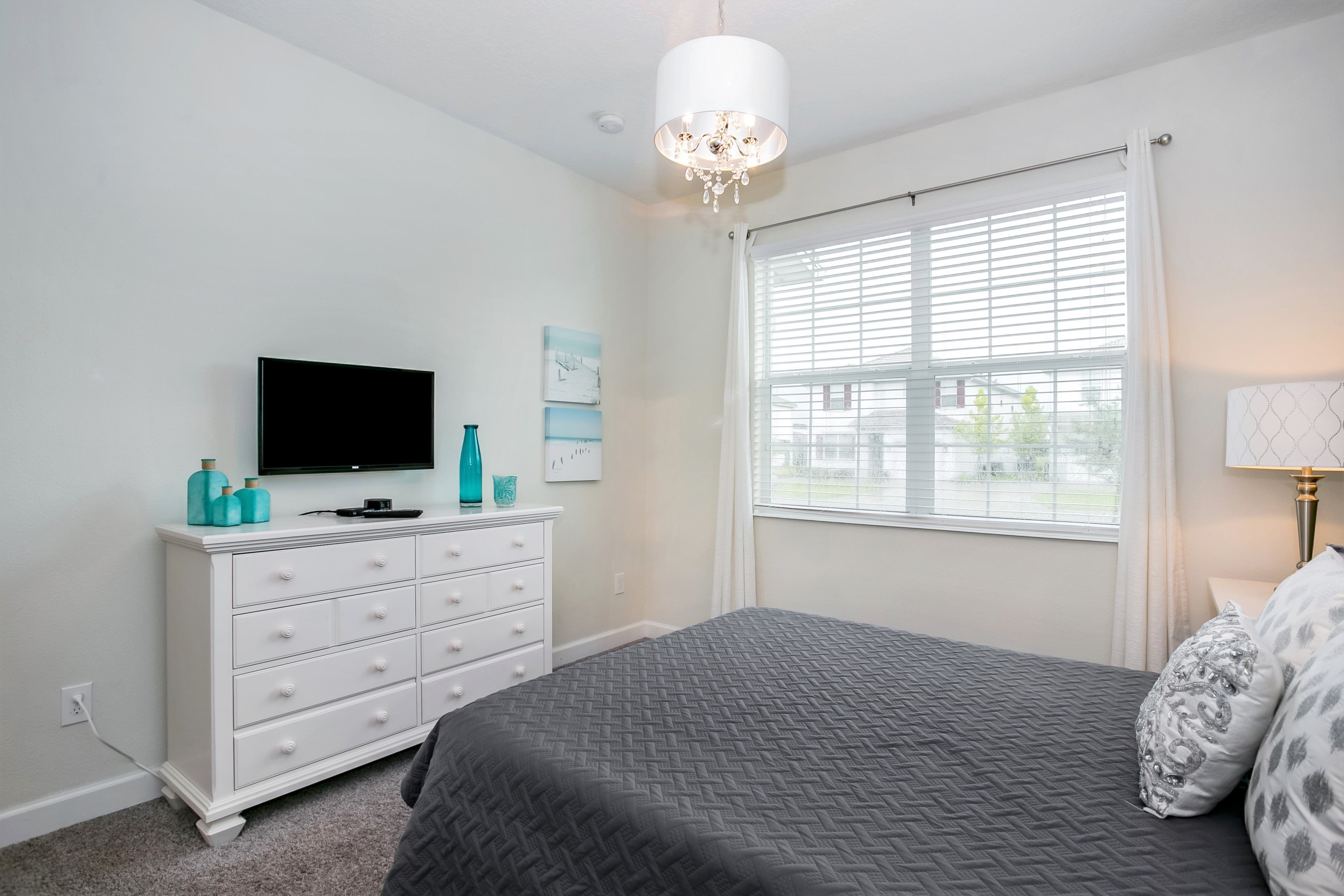 A bedroom with a bed, a dresser, a television, and a window with blinds.