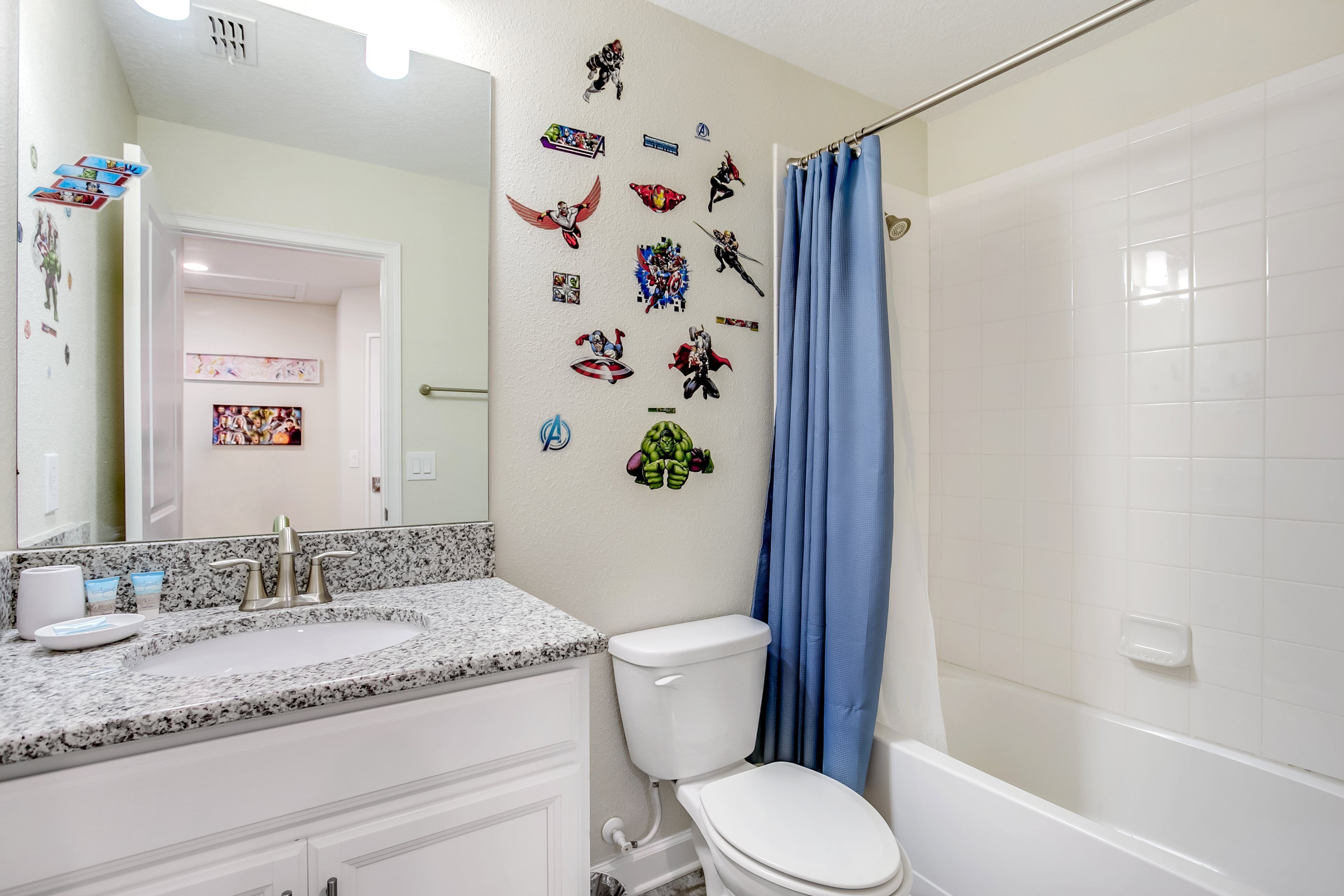 A bathroom with a white toilet, a sink with a granite countertop, and a shower with a blue curtain.
