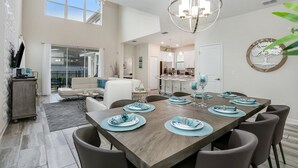A spacious dining area with a wooden table set for six, a chandelier, and a view into the living area. - 5 Bed 4 Ba Villa with Game Room, Pool & Spa (Kissimmee)