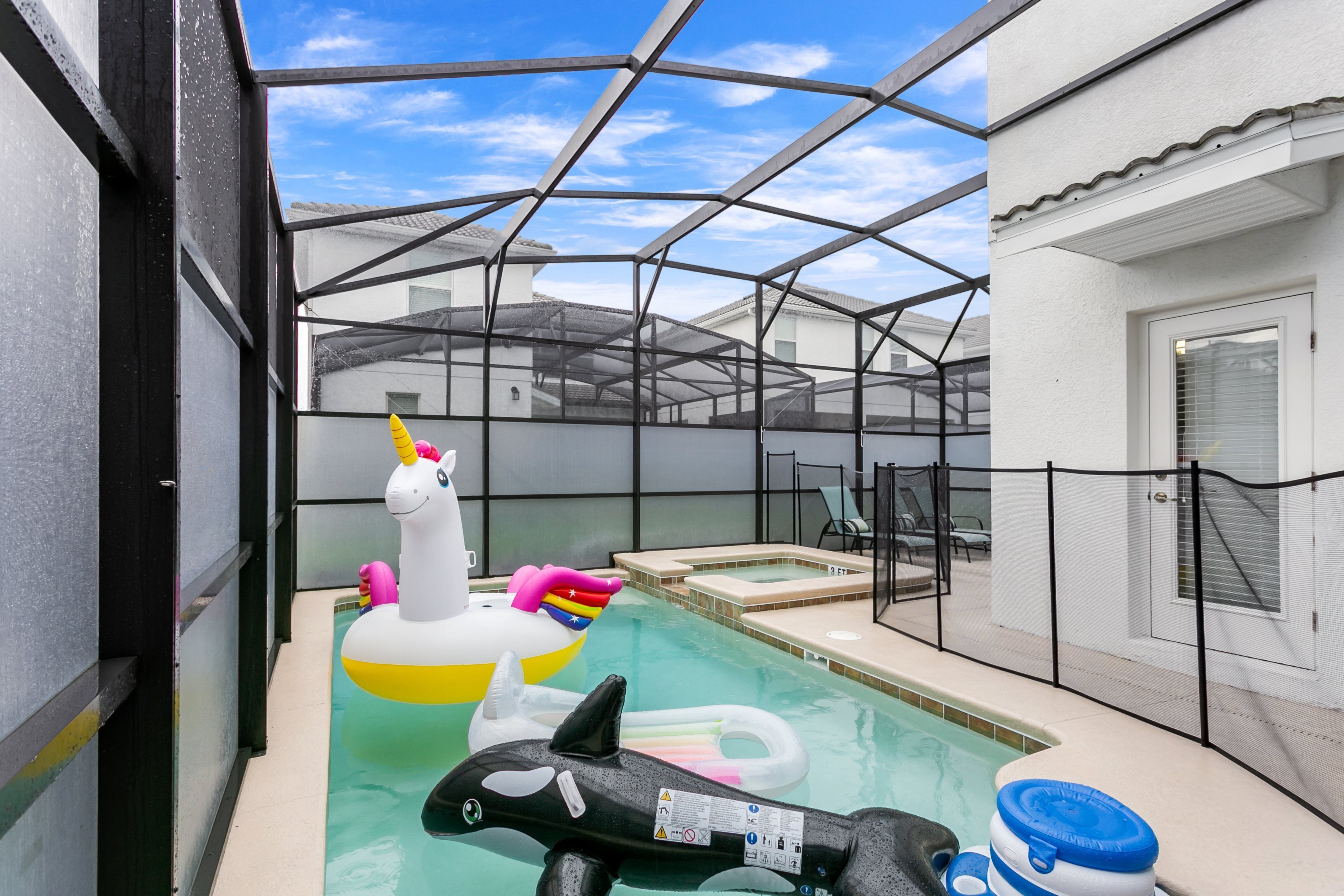 A pool with inflatable unicorn and shark toys, a hot tub, and a covered area with a view of the surrounding buildings.