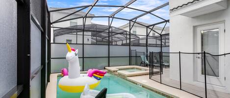 A pool with inflatable unicorn and shark toys, a hot tub, and a covered area with a view of the surrounding buildings.