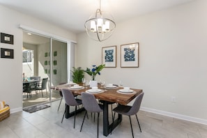 A dining area with a wooden table set for six, surrounded by grey chairs. There is a potted plant with blue flowers on the table, and framed artwork on the wall. - 4bed 3Ba Champions Gate Pool Home (Kissimmee)