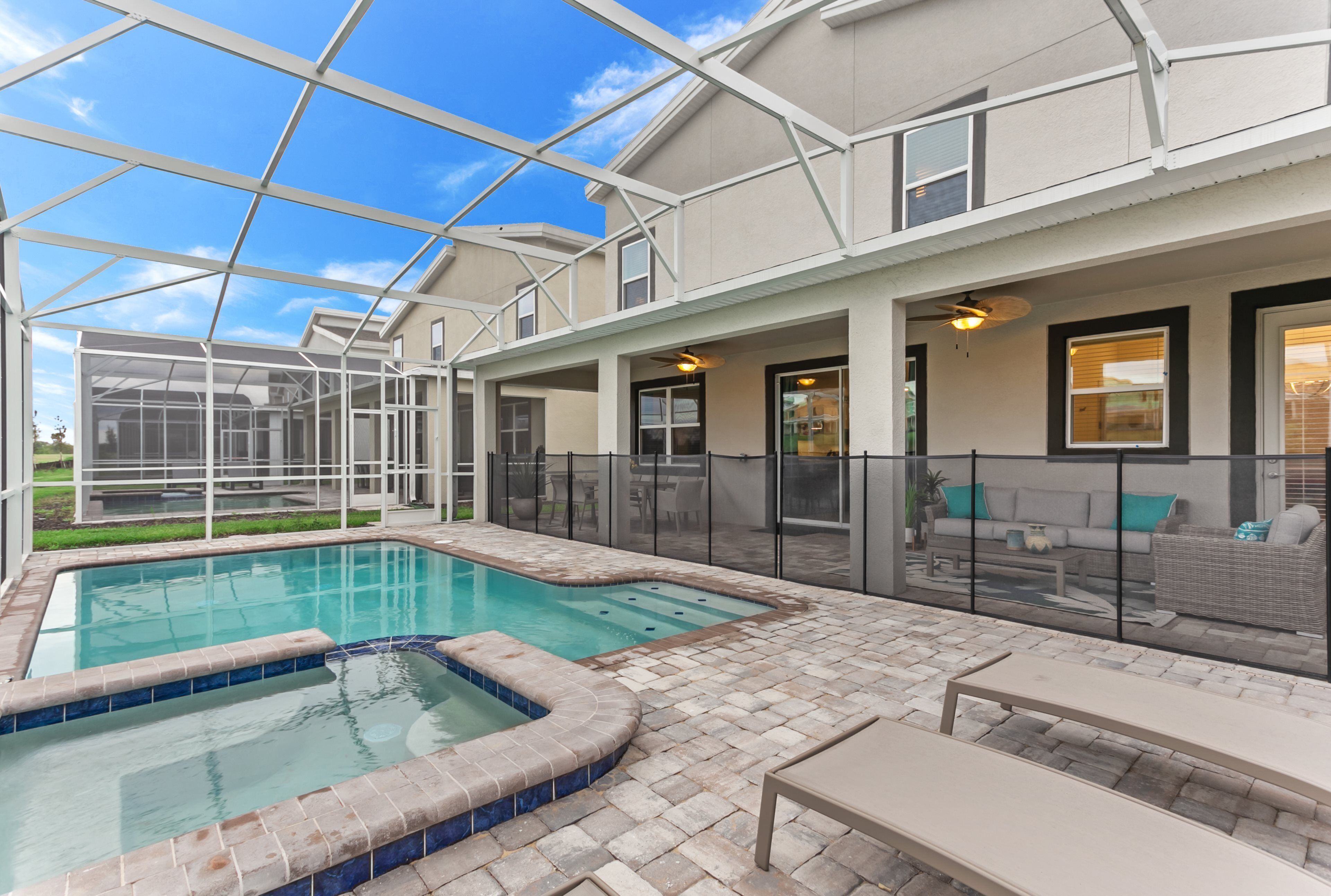 A covered outdoor swimming pool with a hot tub, surrounded by a patio area with seating and a glass enclosure.