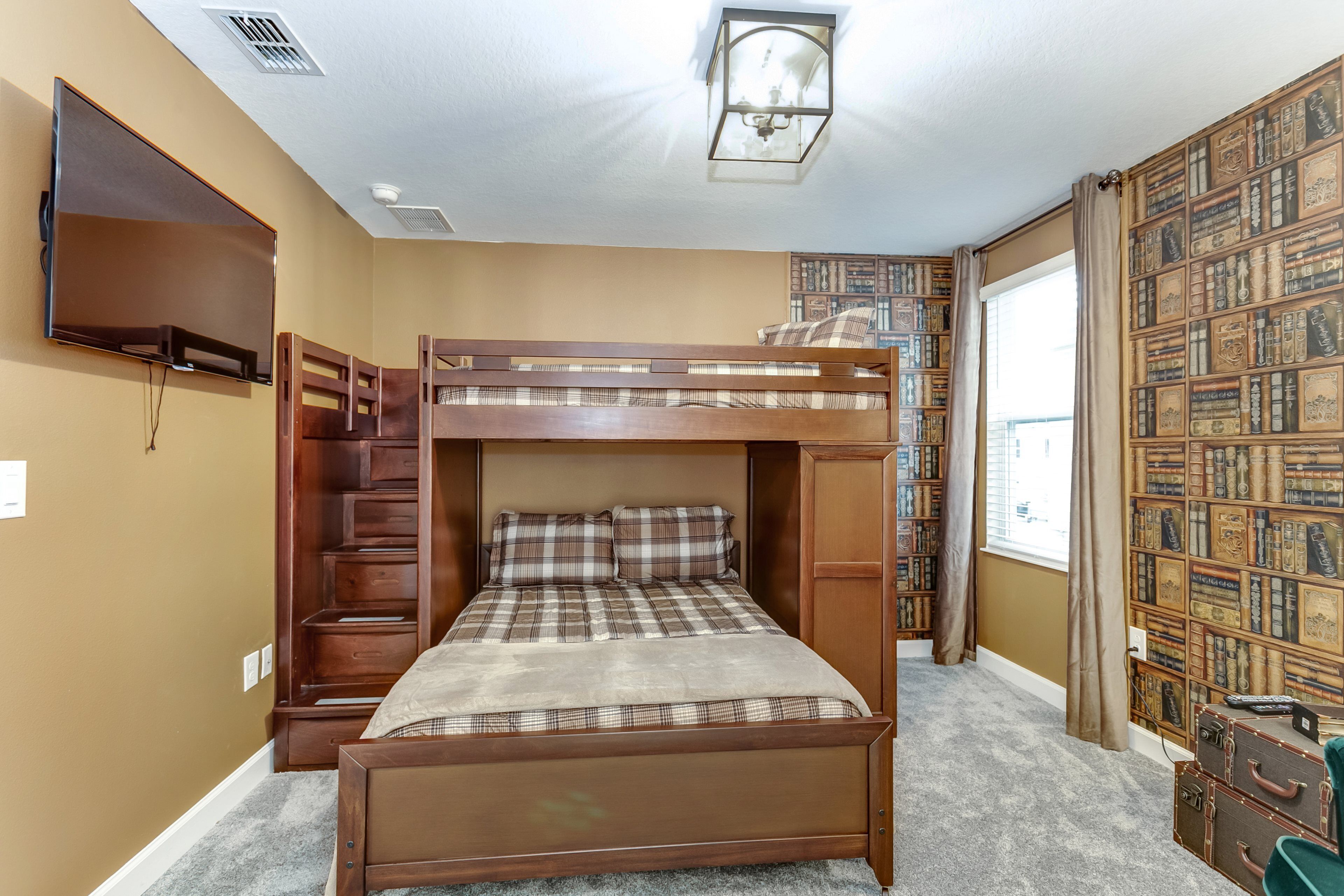 A bunk bed room with a TV, bookshelf, and a window with curtains.