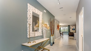 A hallway with a marble floor, a white ornate mirror, a gold console table, and tall vases with dried branches.