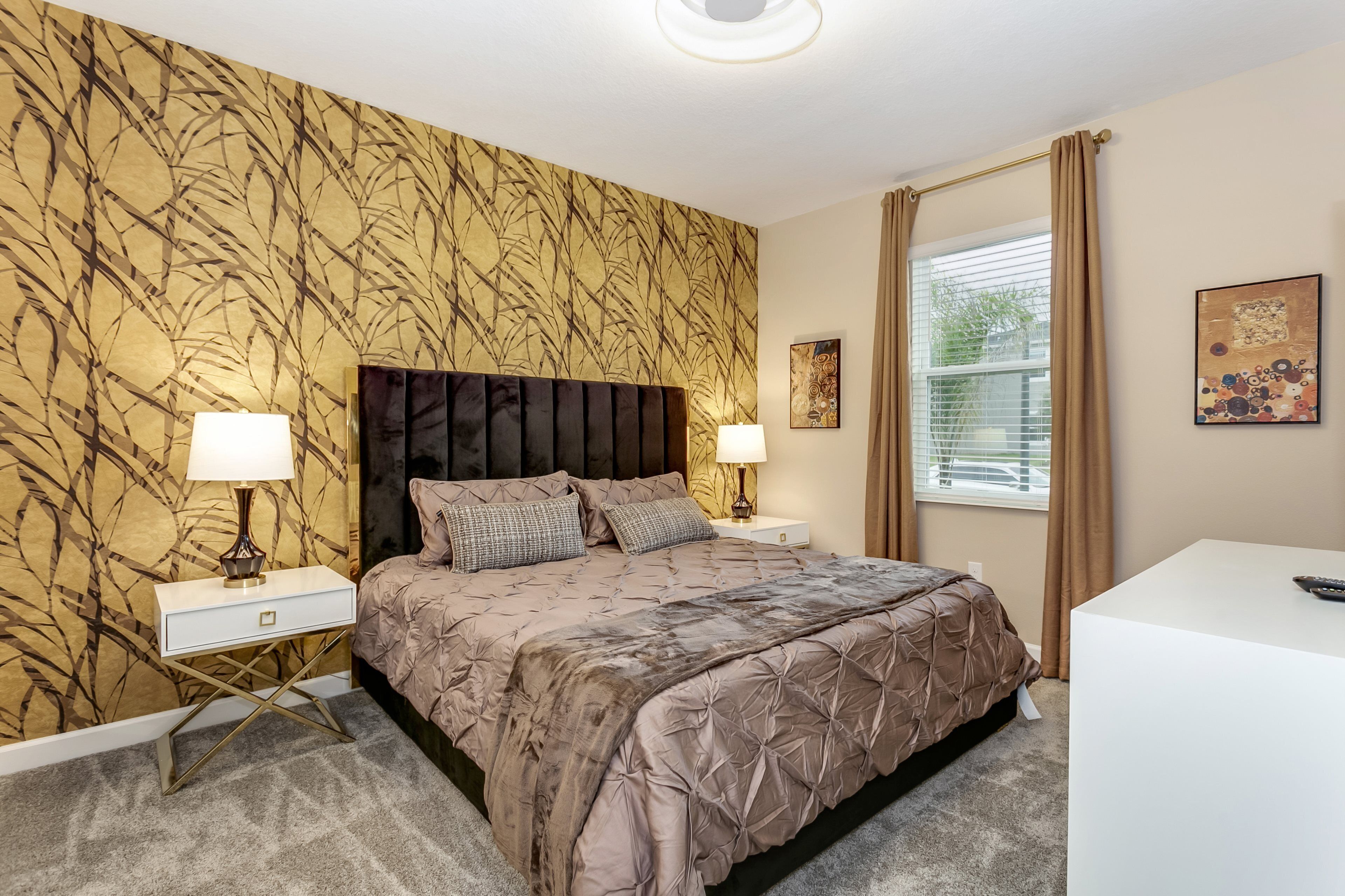 Ein Schlafzimmer mit einem großen Bett, zwei Nachttischen mit Lampen, einem weißen Schreibtisch und einem Fenster mit Vorhängen.