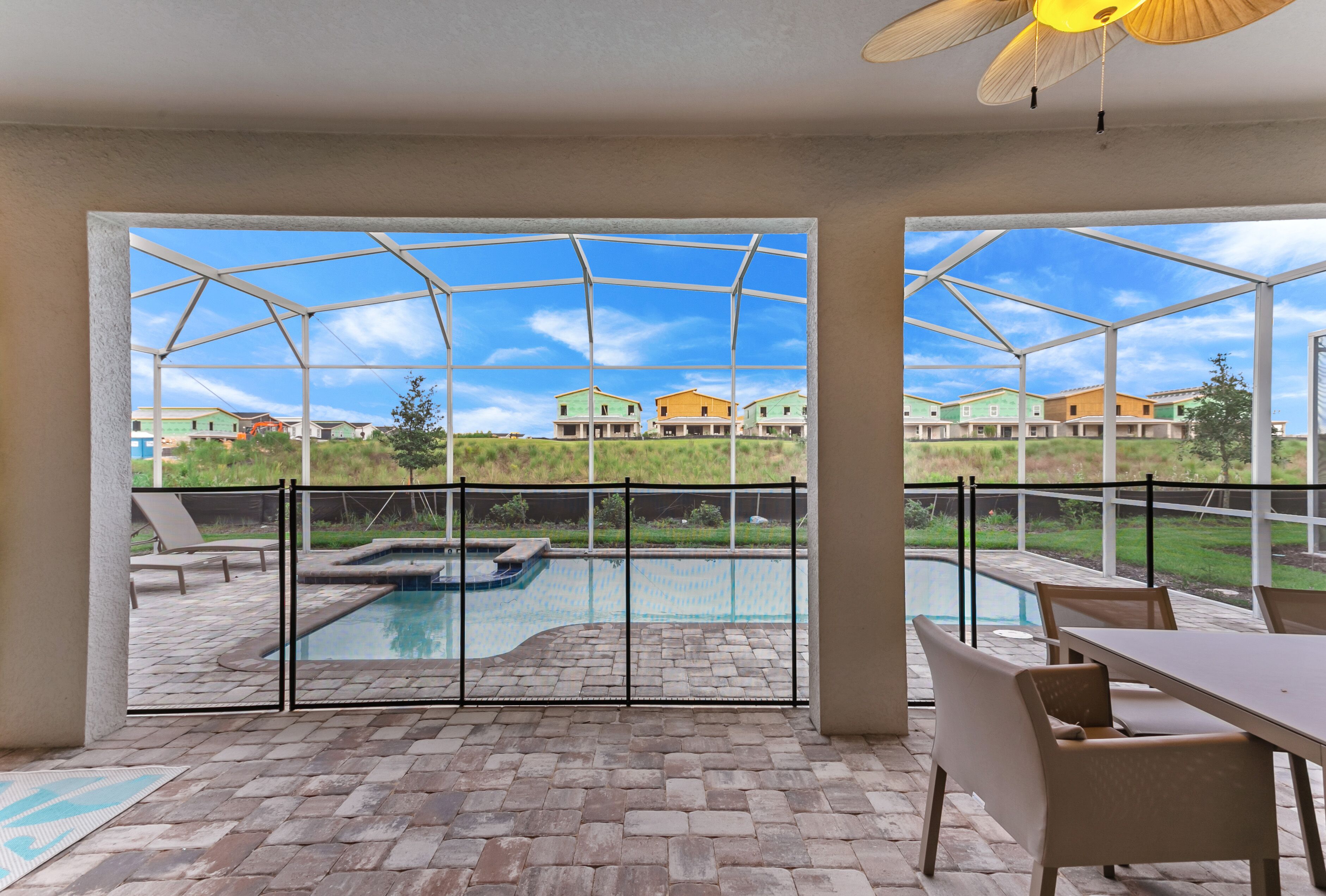 Un espacio exterior techado con piscina, mobiliario de patio y vistas a casas al fondo.