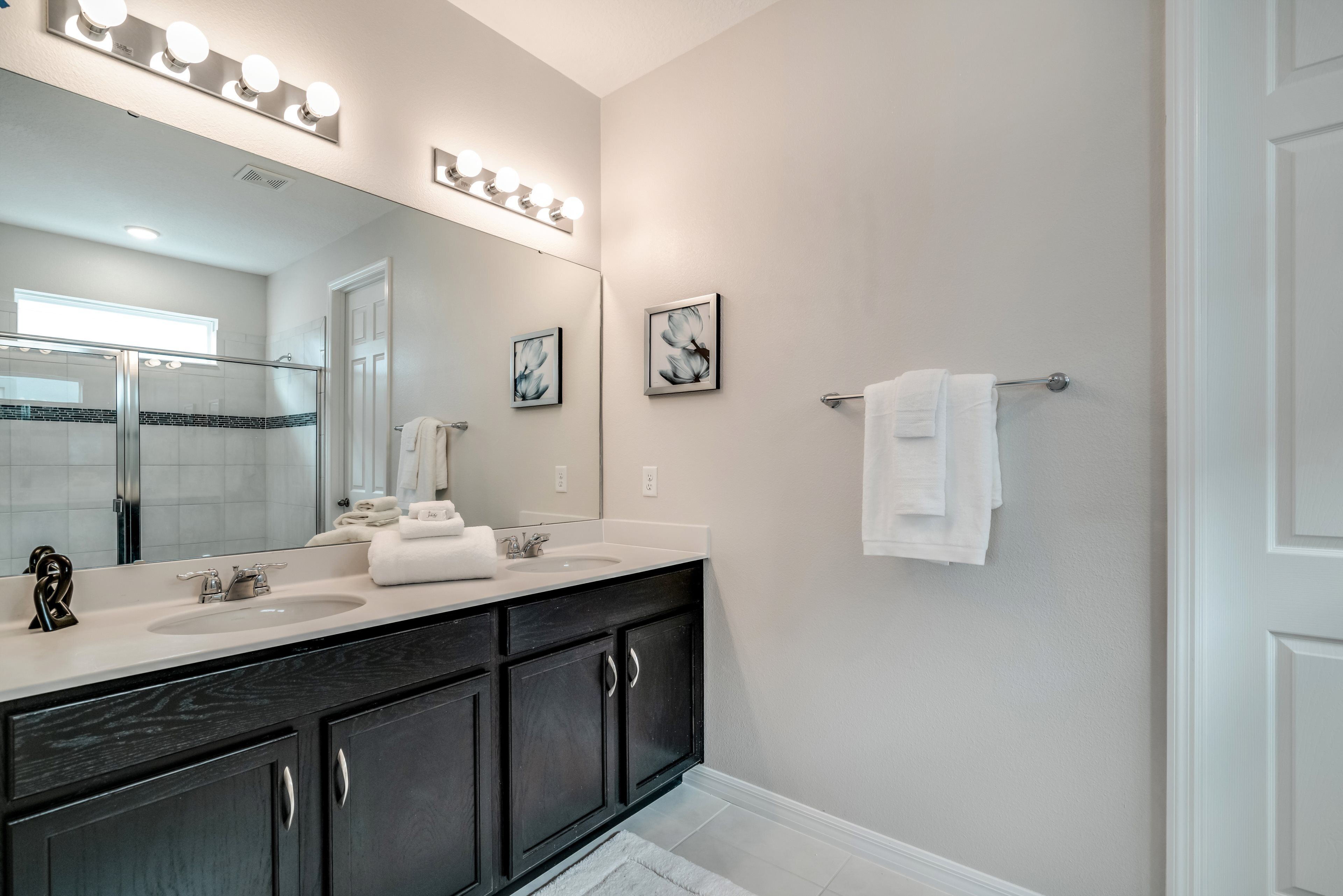 A bathroom with a large mirror, two sinks, dark cabinets, and a towel rack.
