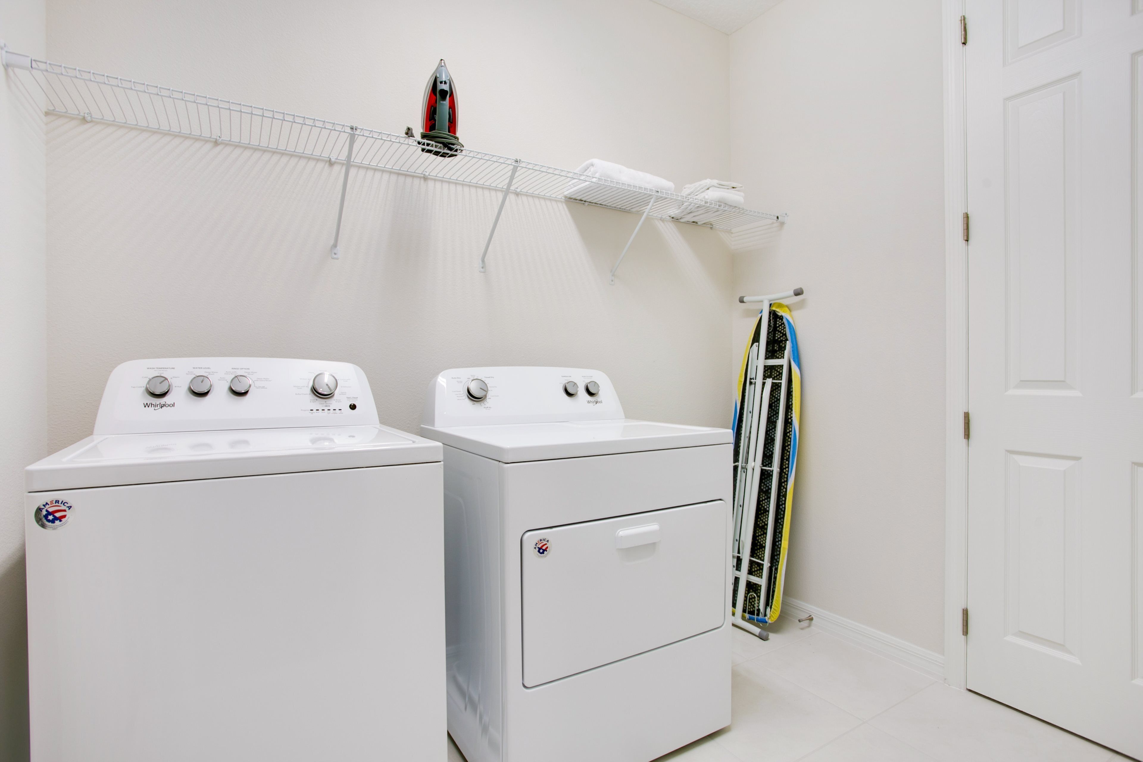 A laundry area with two white Whirlpool washers and dryers, a drying rack, and a door.
