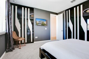 A modern bedroom with a bed, a chair, and a painting on the wall.