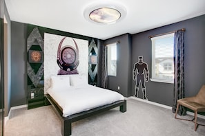 A bedroom with a bed, a chair, a window with curtains, and a wall with a geometric design and a large poster. - Fabulous 8 Bed Villa Pool & Spa, Movie Theater 1805c (Kissimmee)