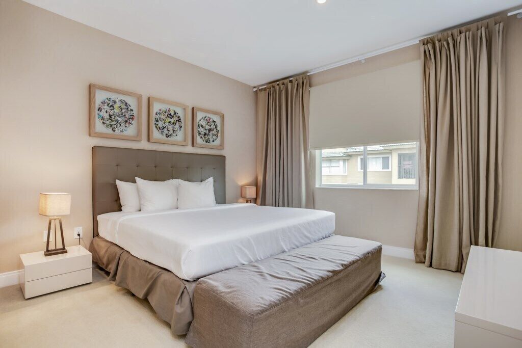 Une chambre d’hôtel avec un grand lit, une table de chevet avec une lampe et trois tableaux encadrés accrochés au mur.