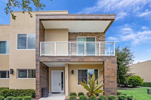 A modern two-story building with a balcony, a door, and a small garden area. - 7577brooklin (Kissimmee)