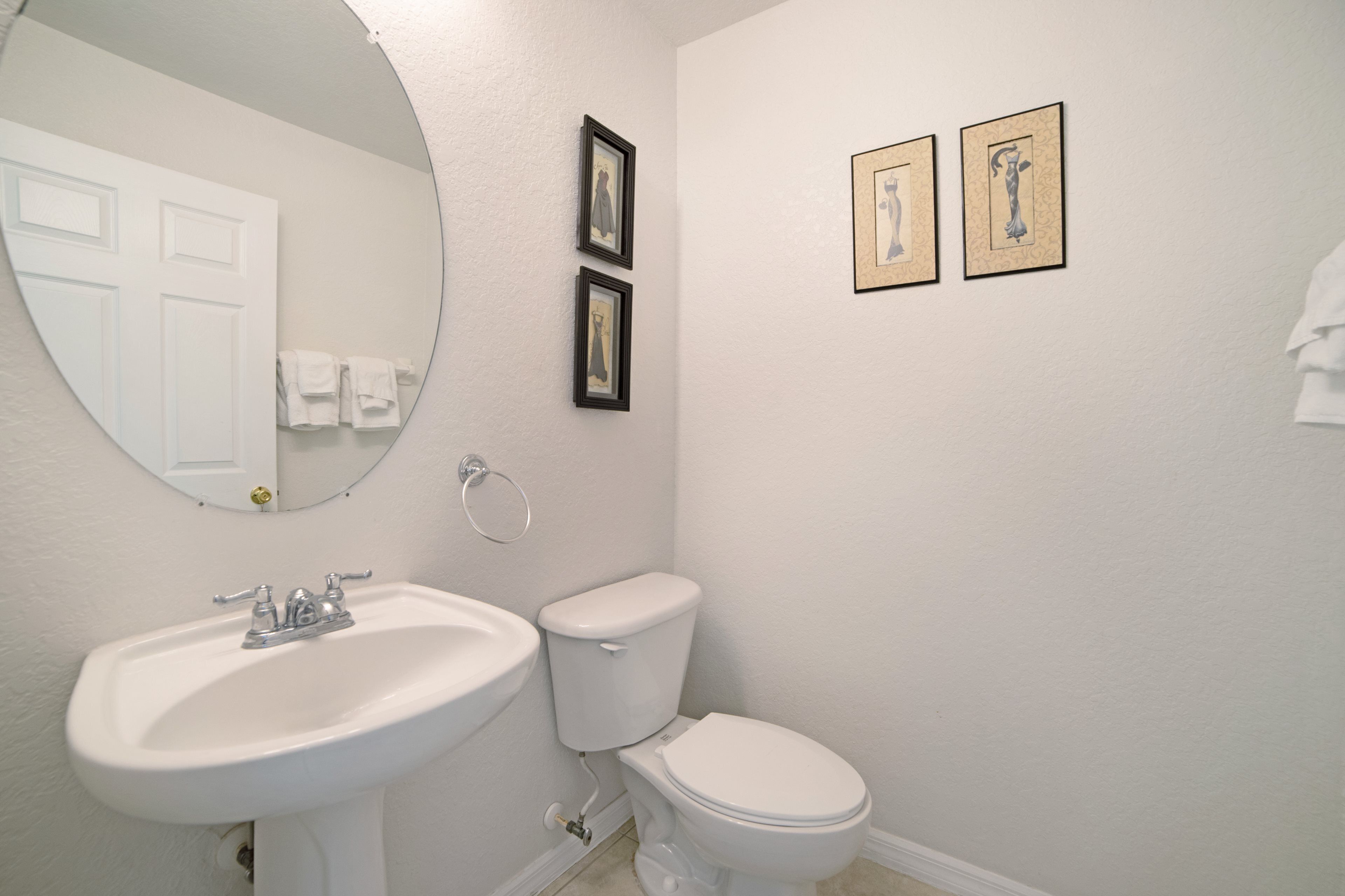Un baño con lavamanos blanco, inodoro y dos cuadros en la pared.