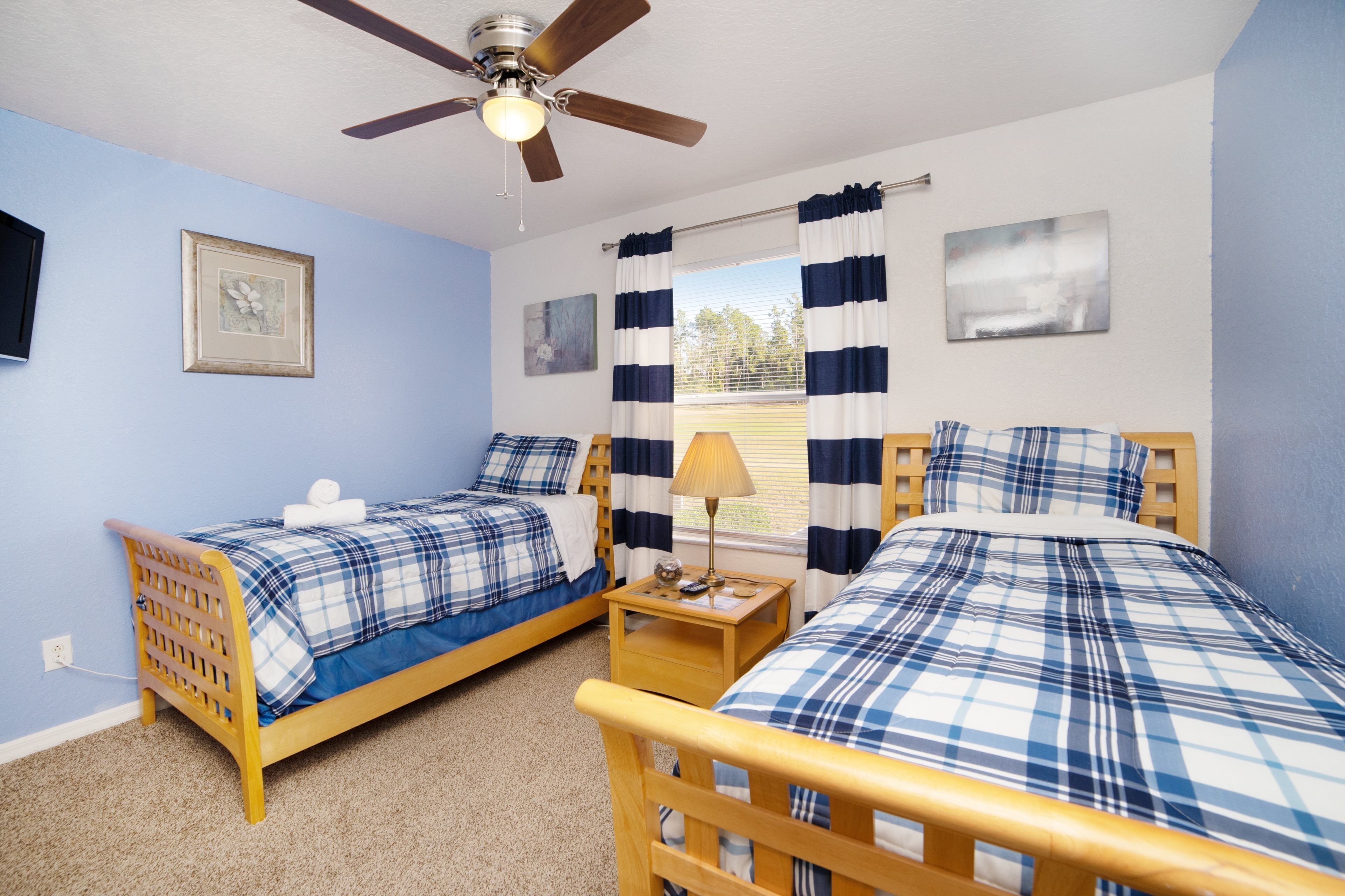 A bedroom with two wooden beds, a ceiling fan, and a window with striped curtains.