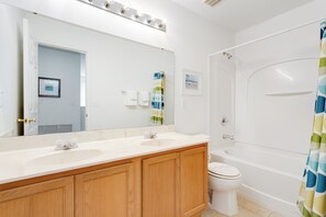 Une salle de bain avec un meuble-lavabo à deux vasques, un grand miroir, des toilettes et une baignoire.