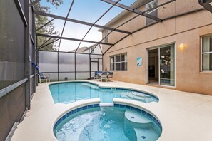 Une piscine entourée de parois en verre, un patio couvert et une porte donnant accès à un bâtiment.
