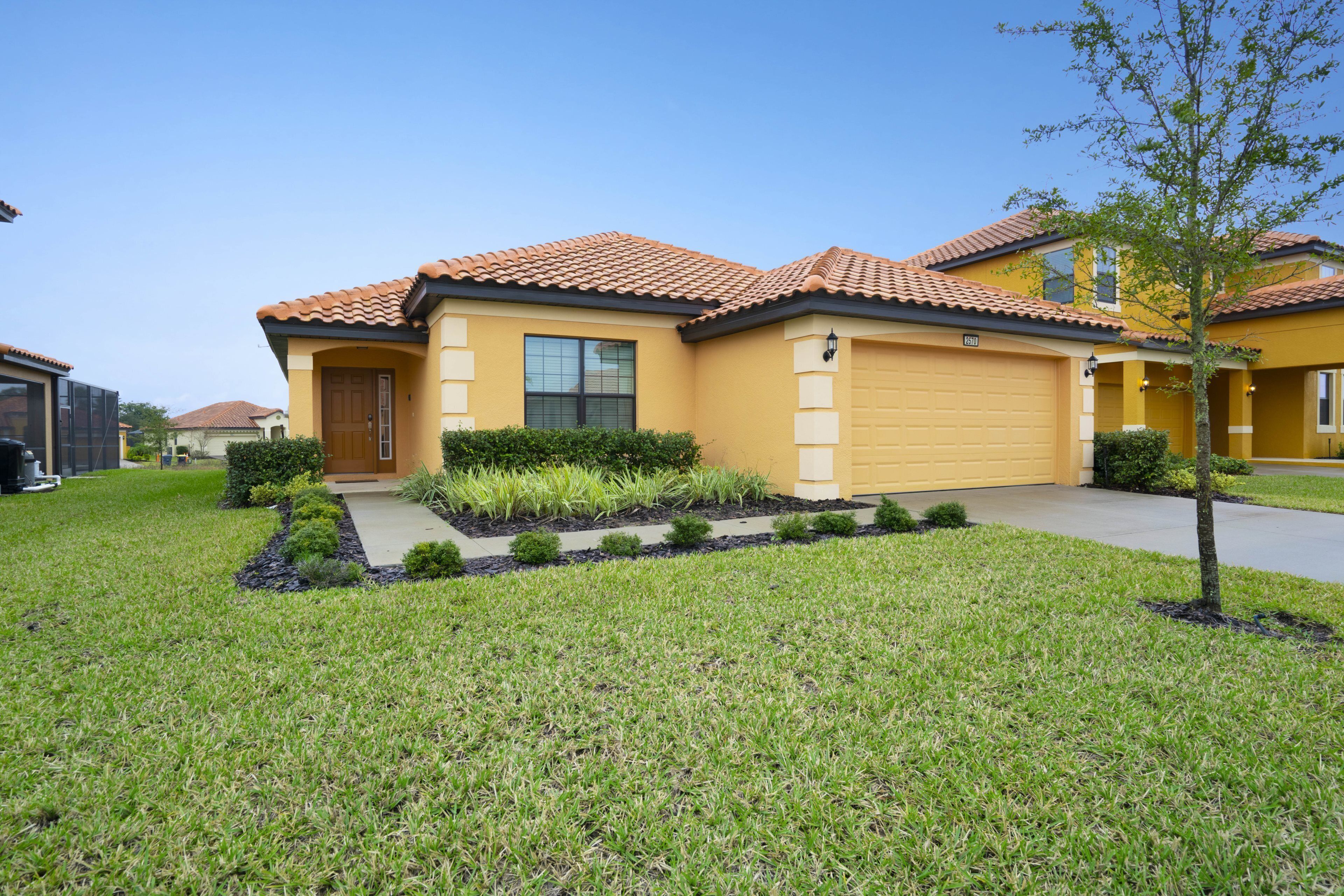 A yellow house with a tiled roof, a garage, and a well-maintained lawn.