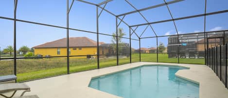 Una piscina cubierta al aire libre con vistas a una casa amarilla y un césped verde.