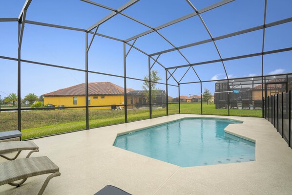 A covered outdoor swimming pool with a view of a yellow house and a green lawn.