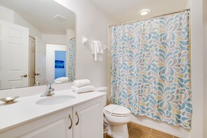 A bathroom with a white sink, a toilet, and a shower curtain with a leaf pattern.