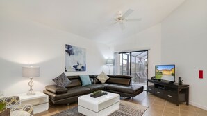 A modern living room with a sectional sofa, a glass coffee table, a TV on a stand, and a ceiling fan. - 2570rosemont (Davenport)