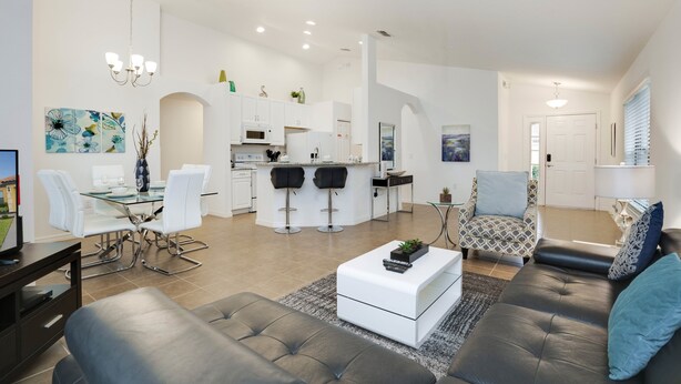 A modern living room with a grey sofa, a coffee table, and a dining area with a glass table and white chairs. - 2570rosemont (Davenport)