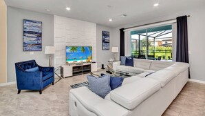 A modern living room with a white sectional sofa, a blue armchair, and a flat-screen TV. - 5bed 4.5ba Villa Games Pool (Davenport)
